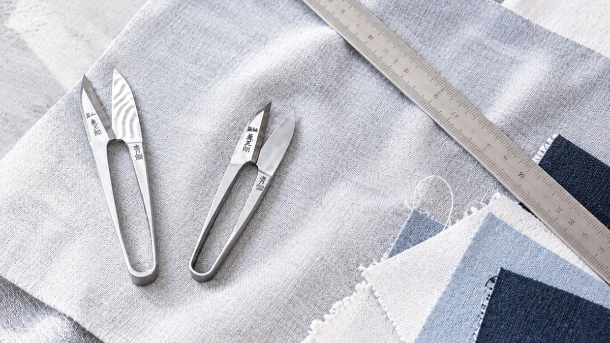 Japanese thread snips on light gray and blue fabric with a measuring ruler and fabric swatches